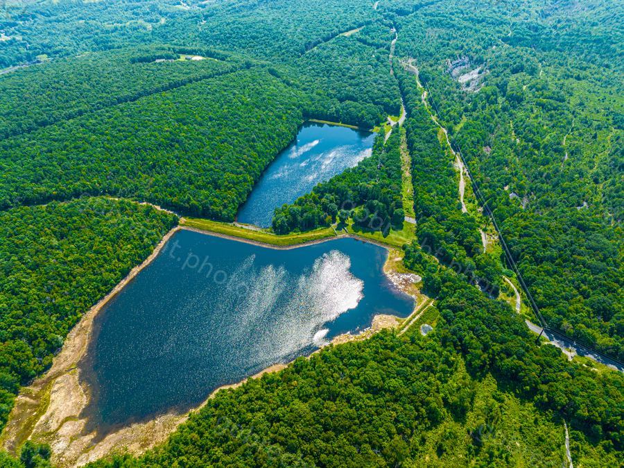 Aerial view of two blue lakes surrounded by dense green forest under afternoon light.