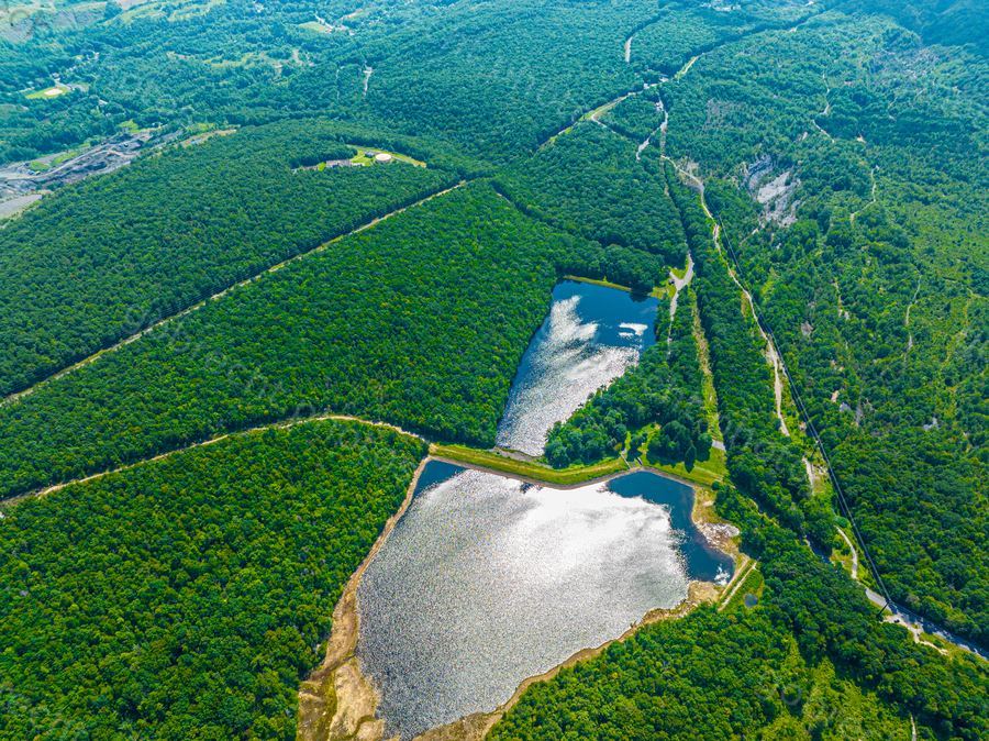 Aerial view of two reservoirs nestled in dense forest with winding rivers, captured in afternoon light.