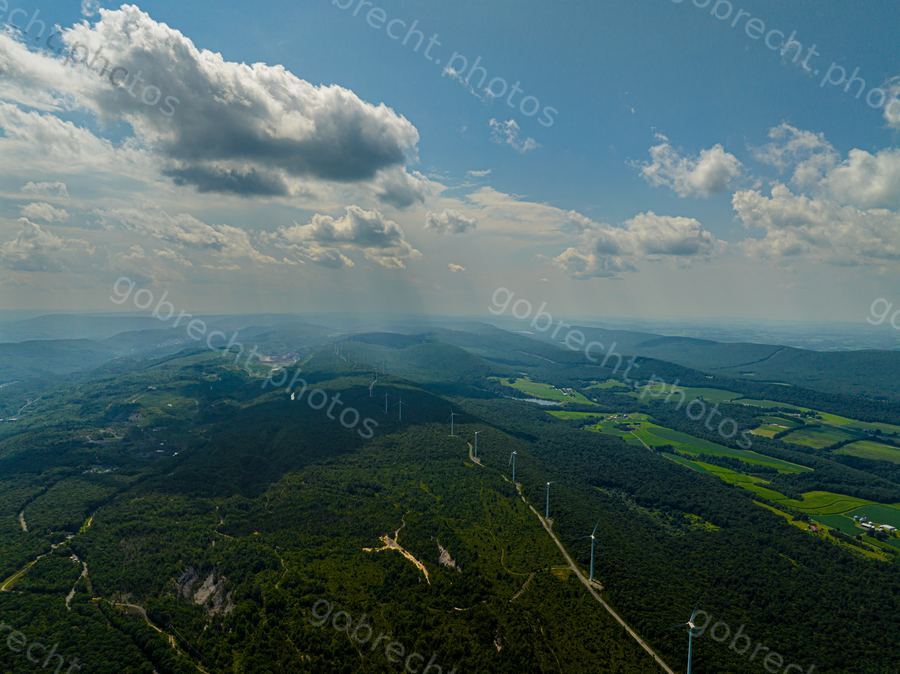 Aerial view of forested mountains with transmission towers and valleys under afternoon sunlight.